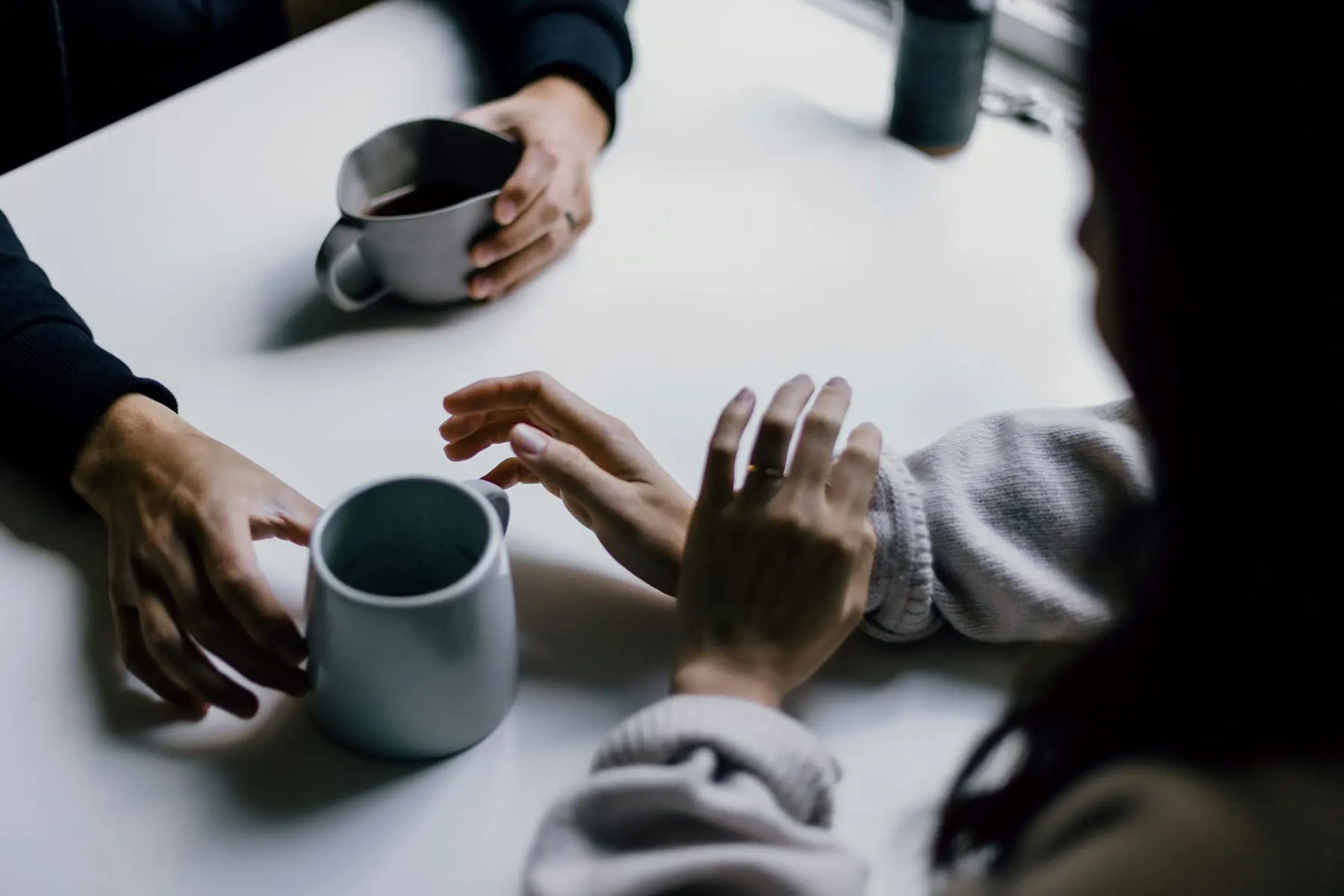 Hænder omkring kaffekopper under en rolig samtale